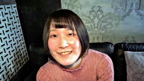 Cute Asian teen model smiling happily in frilly pink sweater on couch