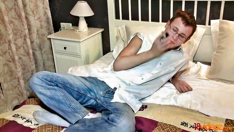 Slim redhead guy in jeans lounging on bed, smoking and eyeing girl for hot surprise