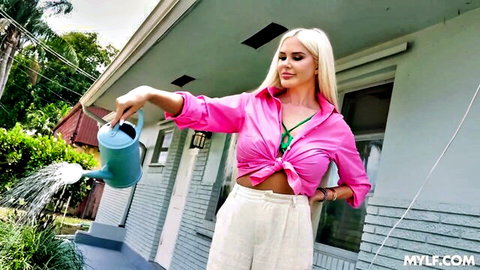 Blonde MILF neighbor watering plants outdoors in revealing pink blouse showing cleavage and white pants