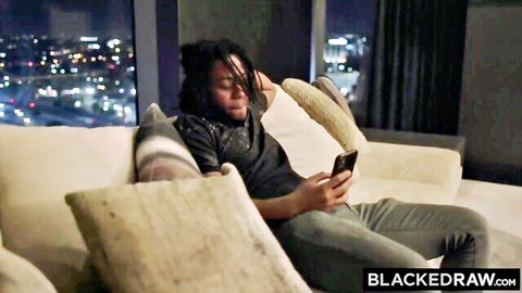 Black man with dreads lounges on couch checking phone in Blacked Raw ebony threesome preview