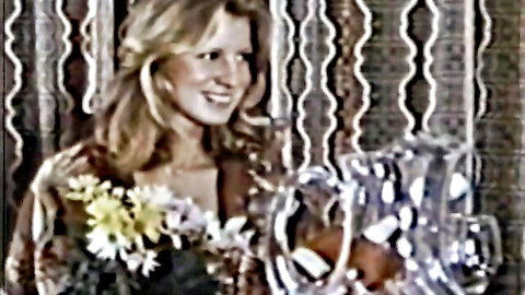 Blonde slim coed smiling with flowers in vintage adult film scene