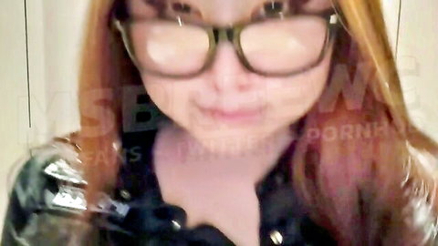 Sexy redhead with glasses smiles teasingly in shiny black latex top