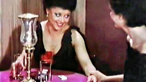 Vintage retro women in black dresses holding hands flirtatiously at romantic candlelit dinner table