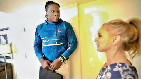 Blonde woman in floral top chats with dreadlocked black man holding briefcase in yellow hallway