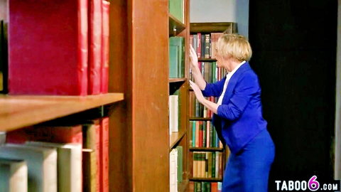 Dee Williams in tight blue suit reaching for books, teasing big tits