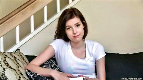 Cute brunette babe in tight white t-shirt sitting on couch smiling teasingly