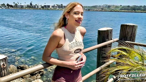 Blonde MILF babe in tight tank top and shorts smiling seductively by the waterfront dock