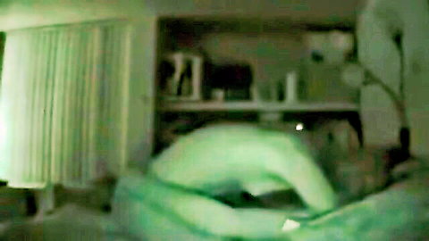Blurry night vision of nude girl bent over on green bed in bedroom