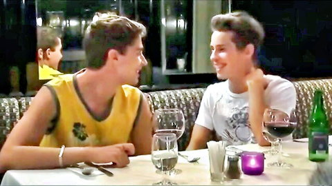 Two young handsome men smiling intimately at romantic candlelit dinner with wine glasses