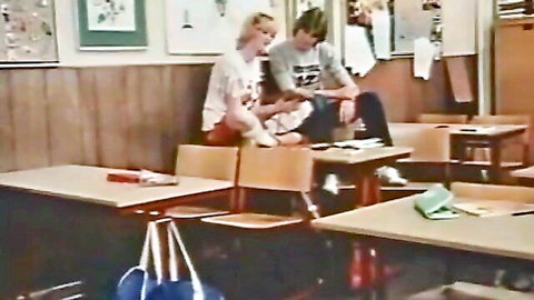 Blonde schoolgirl in white blouse and red skirt with guy in retro classroom scene