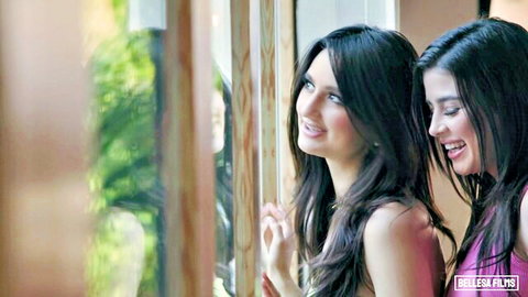 Two skinny tanned brunettes with small tits smiling seductively in pink tops by window
