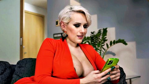 Angel Wicky in low-cut red dress showing deep cleavage on couch