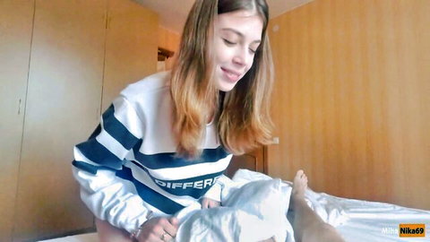 MihaNika69 smiling in striped sweater, leaning forward in POV titfuck tease