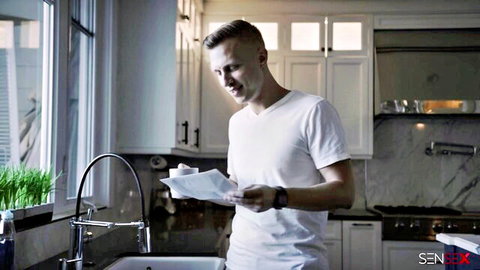 Handsome young white guy smiling in modern kitchen holding papers by sink