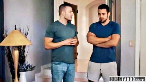 Two muscular men in casual shirts and pants standing face-to-face in modern living room
