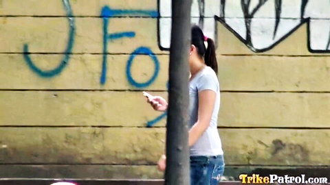 Mercy teases outdoors on Trikepatrol, casual white tee and jeans against graffiti wall