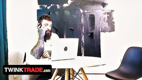 Bearded tattooed guy pondering at desk in Twink Trade gay orgy preview