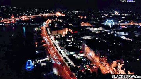 Aerial night view of city skyline with lit bridge, river, buildings and Ferris wheel