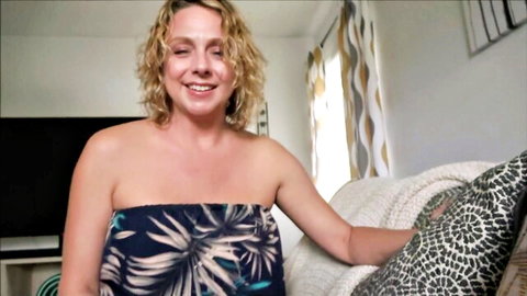 Blonde curvy MILF smiling seductively in strapless floral tube top teasing huge tits on couch