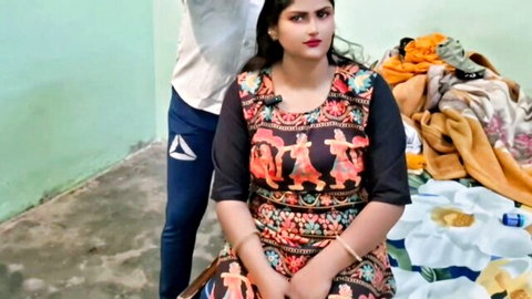 Sexy Indian woman in colorful embroidered dress sits on bed with man standing behind her