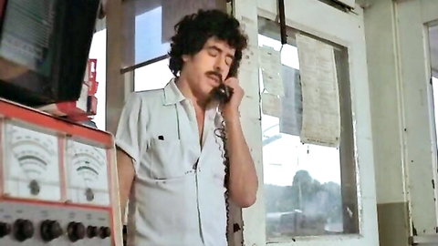 Vintage man with mustache talking on rotary phone in control room with gauges and monitors