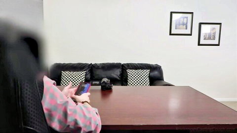 Blurry teen girl in pink checkered top holds phone near camera on table in casting couch room