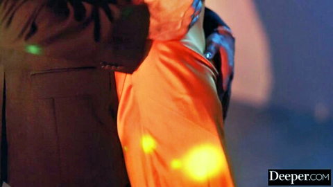 Blurry suited man embraces figure in orange outfit under yellow spotlights on stage