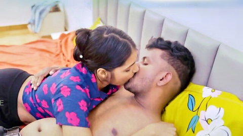 Sexy Indian wife in shorts straddles and passionately kisses muscular shirtless husband's lips on bed.