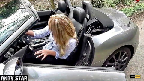 Blonde Andy Star sitting in silver convertible car outdoors, teasing in blouse