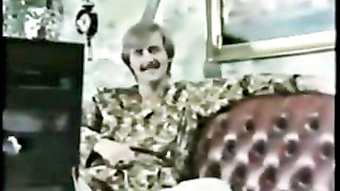 Vintage mustached man in camouflage robe lounging smiling on red couch