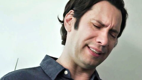Brunette man grimacing in apparent pleasure with squinted eyes and open mouth in blue shirt closeup