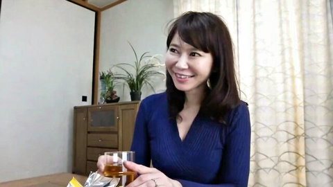 Smiling Japanese mature brunette in tight blue sweater holding whiskey glass seductively