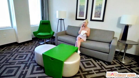 Blonde Lilly Bell in short white dress, seated teasingly on couch
