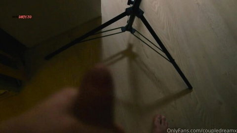 Blurry low-angle shot of tripod on wooden floor with bare foot visible in amateur OnlyFans setup