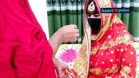 Desi bride in red lehenga veiled and intimate with partner on bed