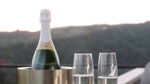 Champagne bottle in ice bucket with two glasses on balcony overlooking scenic sunset hills