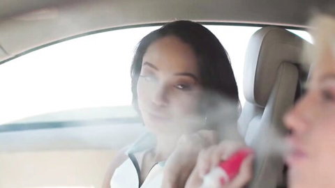 Asian beauty exhaling thick vape smoke seductively towards hot blonde in car backseat