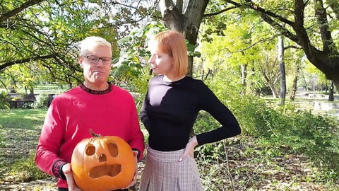 Dolly Dyson in plaid skirt with older cuckold partner holding pumpkin outdoors