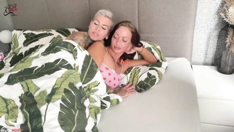 Two tattooed lesbians in pink lingerie cuddling seductively on bed with cleavage exposed