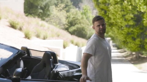 Handsome buzzed man in white tee leans on black convertible sports car outdoors on sunny day