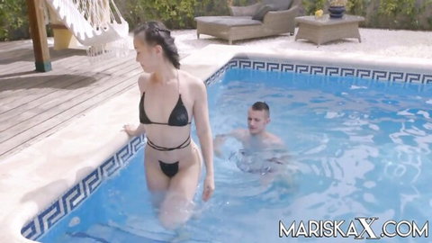 Slim brunette in black bikini teases at pool edge with man in water