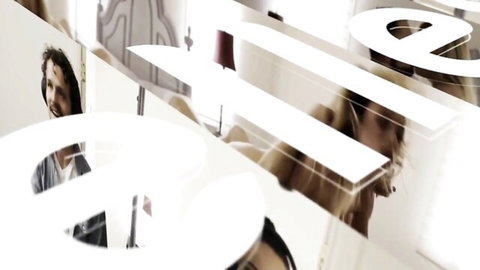 Smiling curly-haired man in shirt behind bold white ELLE magazine logo overlay