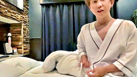 Cute East Asian boy in open white robe exposing smooth chest sitting on bed