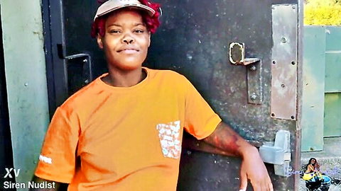Smiling ebony babe in orange XV t-shirt leans on trailer door