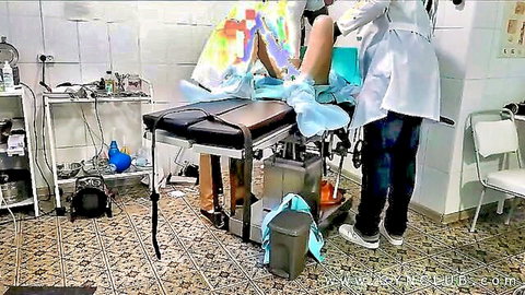 Doctor in white coat examines exposed shaved pussy of patient with legs spread in gyno stirrups