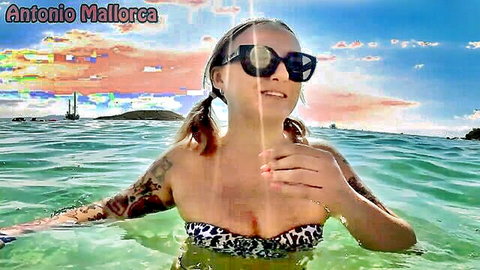 Tattooed blonde babe with big tits in leopard bikini smiling sexy in Mallorca beach waters