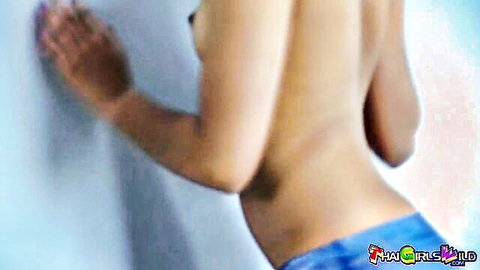 Topless Thai gogo dancer leaning against wall in blue shorts, back view