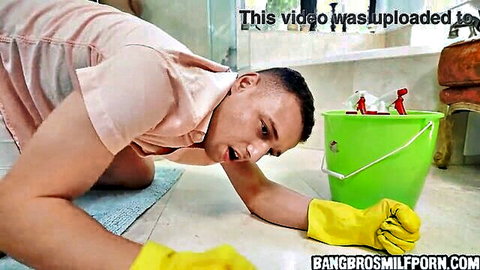 Surprised stepson in pink shirt and yellow gloves kneeling by green cleaning bucket on bathroom floor