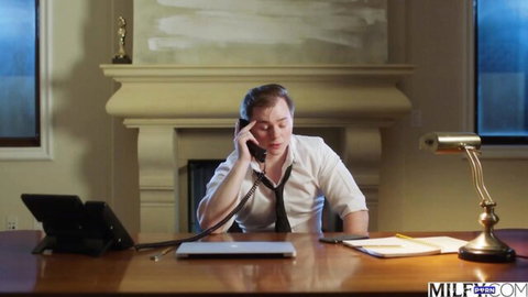 Young businessman in white shirt and tie talks on phone at desk in luxurious office