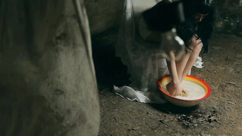 Sensual brunette in white gown squats dipping hands in creamy milk bowl teasing thighs erotically